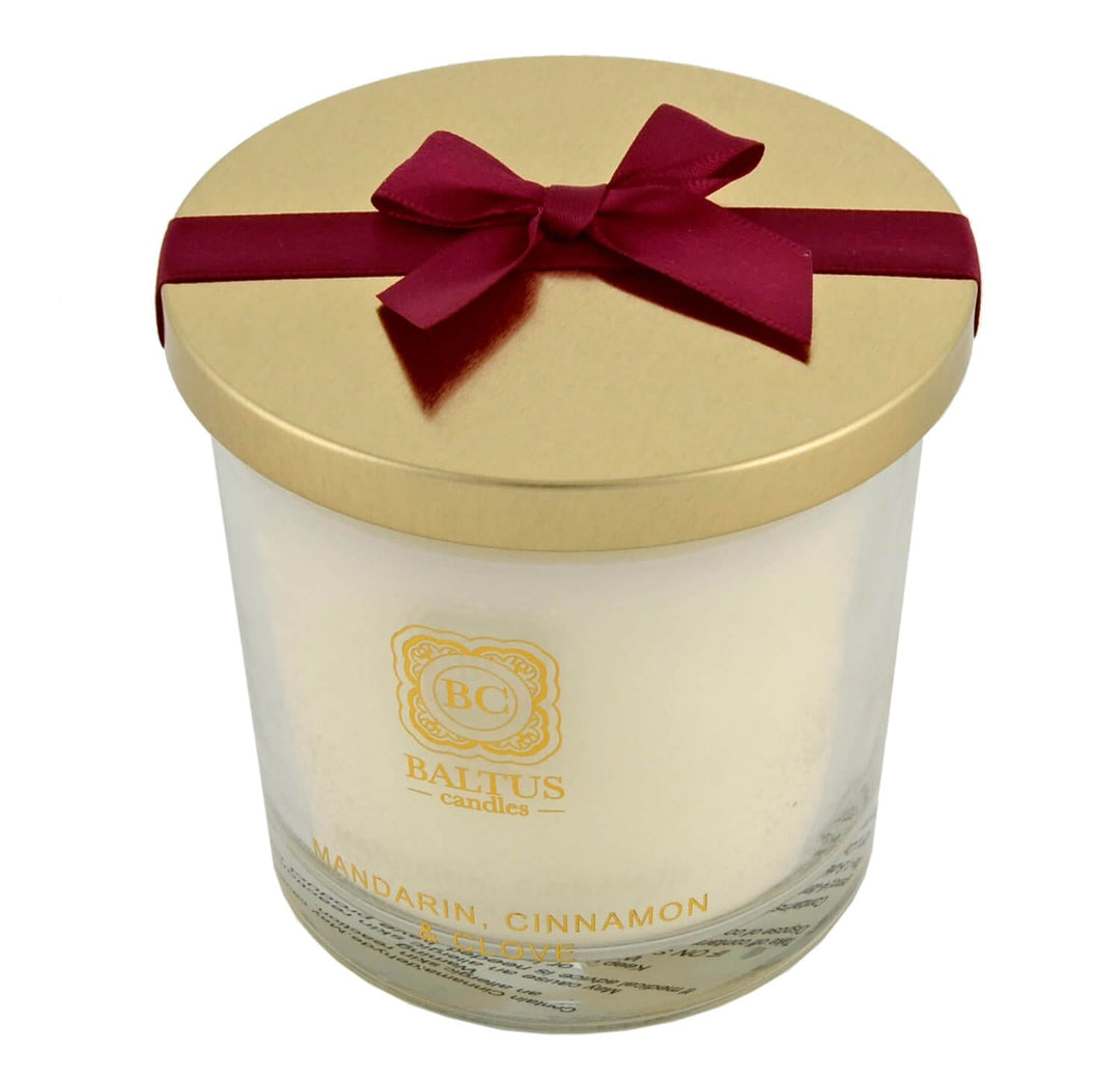 Candle with a gold lid and red bow, and Baltus branding.
