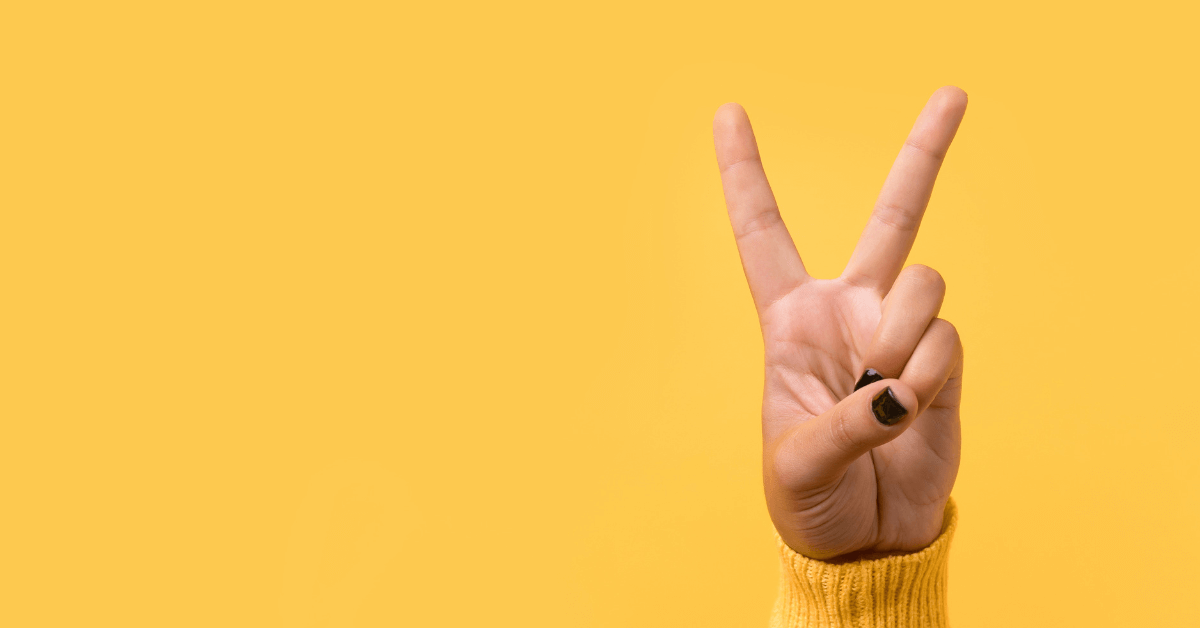 person's hand doing peace sign against bold yellow background