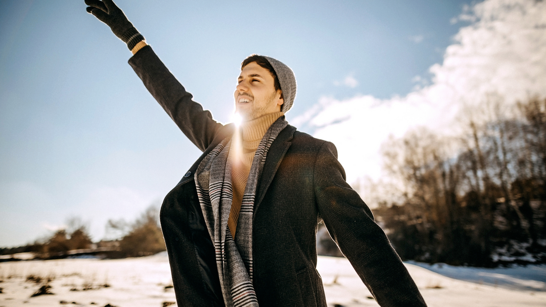 happy man in snow outdoors wearing hat, scarf and glove set