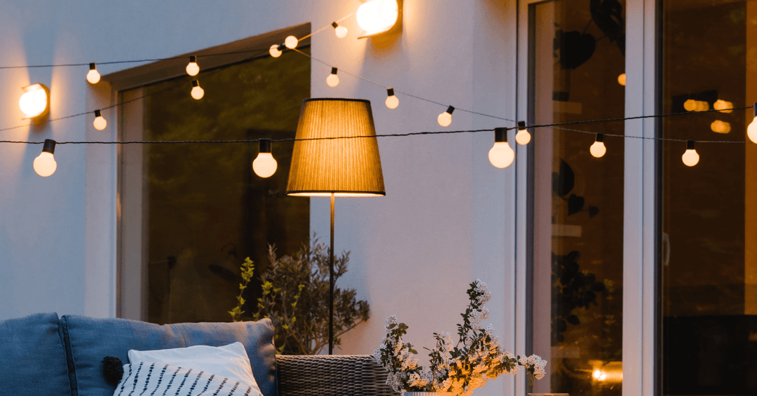 warm white string lights in garden space hanging from wall with sofa set underneat and large patio windows in the background