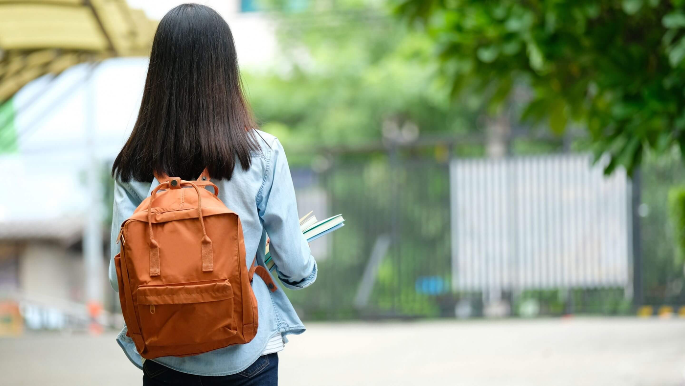 university student carrying books and wearing an orange backpack
