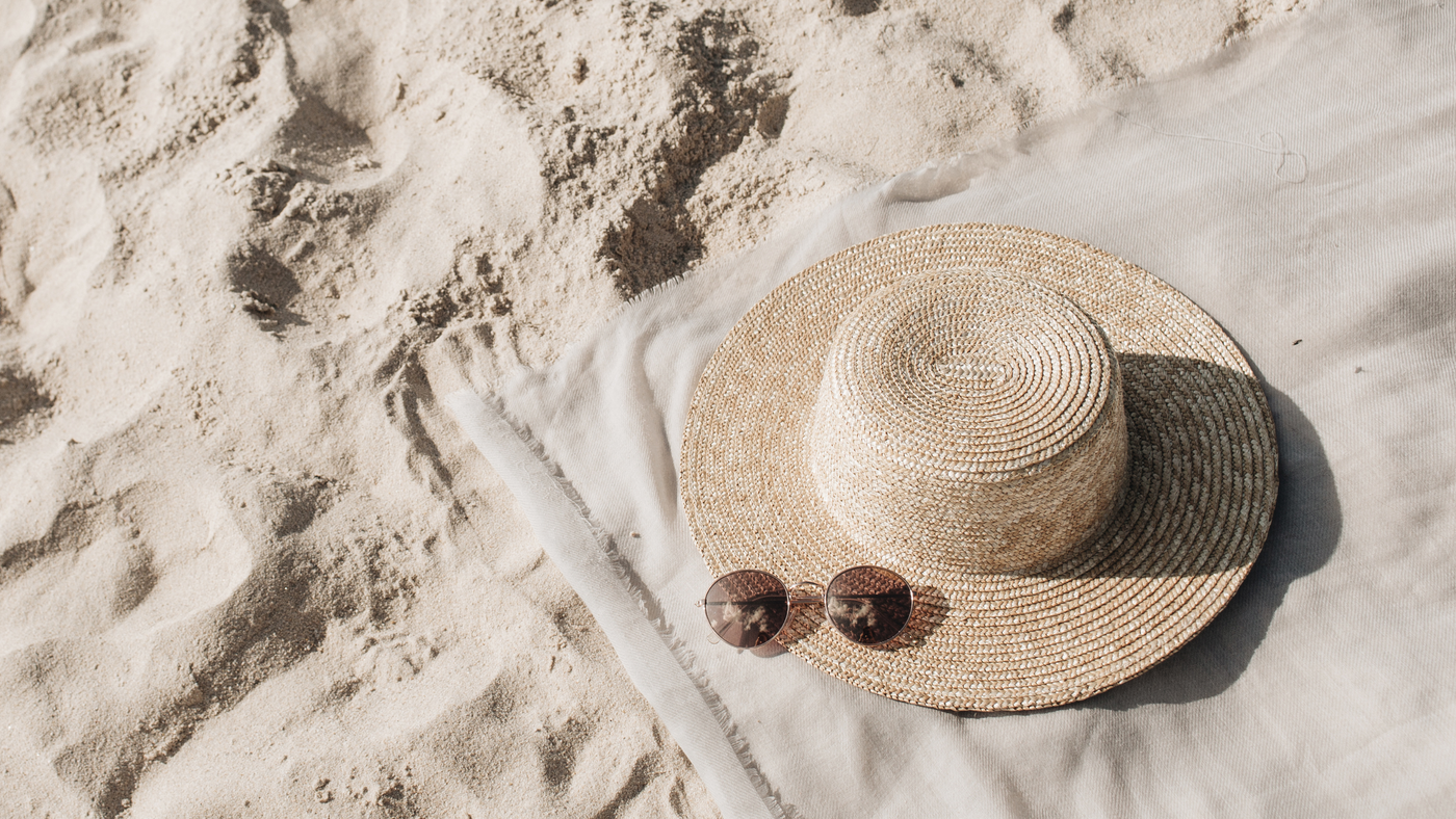 straw summer hat on beach towel on sand with sunglasses