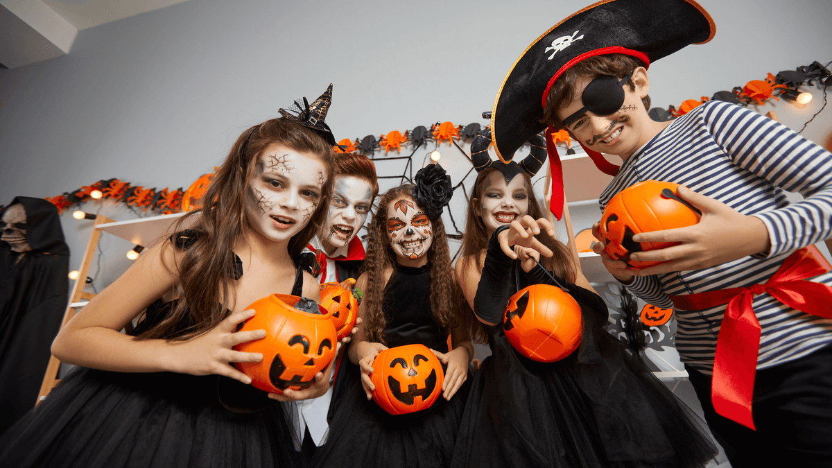 group of kids posing for the camera holding pumpkin treat jars - dressed up for halloween, pirate, witch, vampire