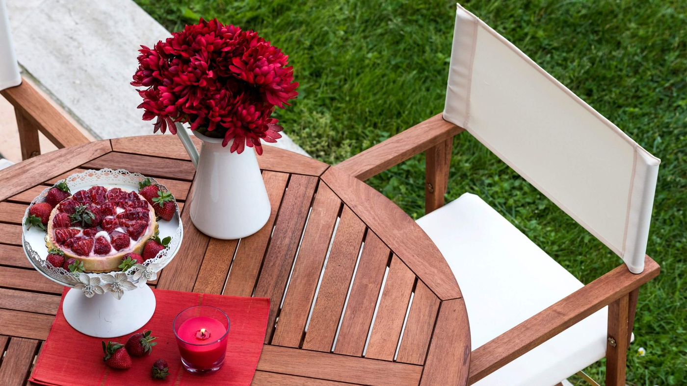 top view of wooden garden dining table and chair with red flowers and candle to decorate