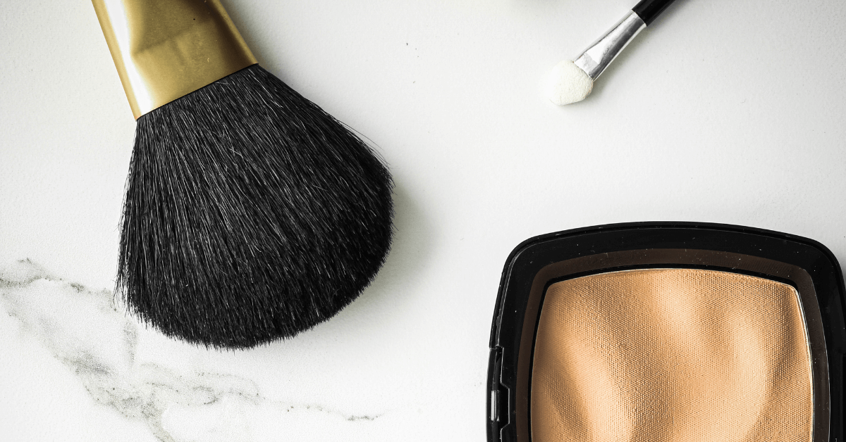 make up brush with black coloured bristles on marble worktop beside concealer powder pallete