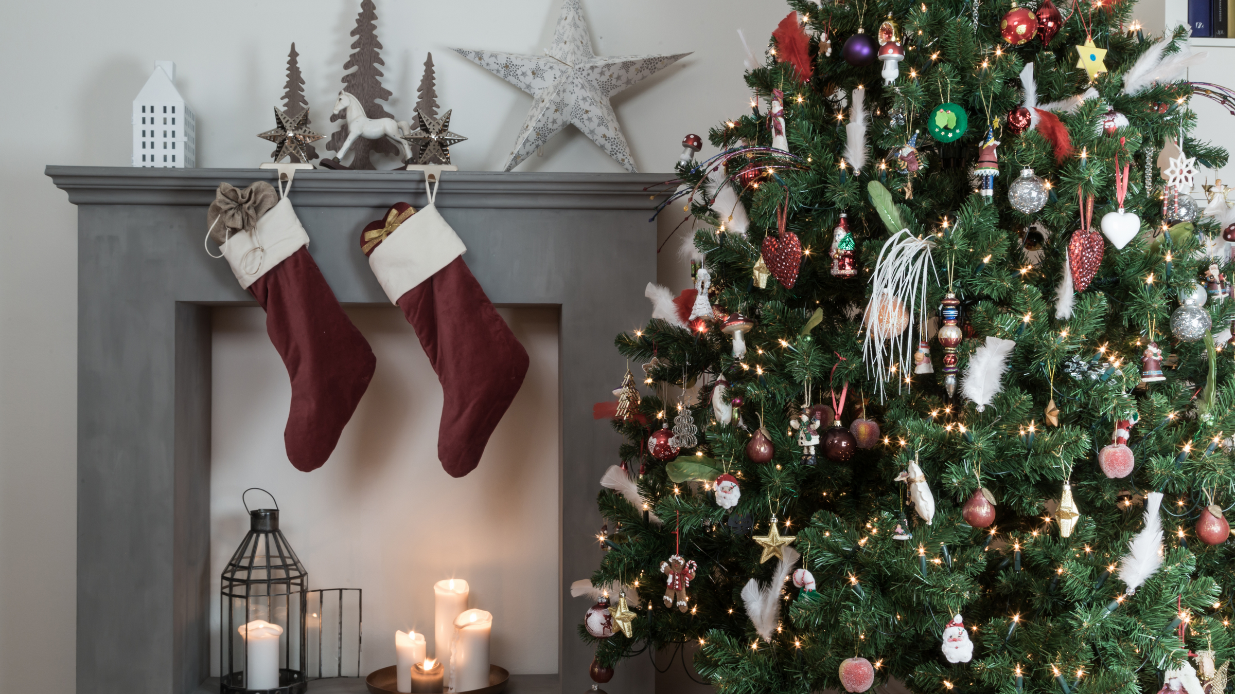 pre-lit christmas tree beside grey fireplace decorated with wooden christmas decorations and stockings