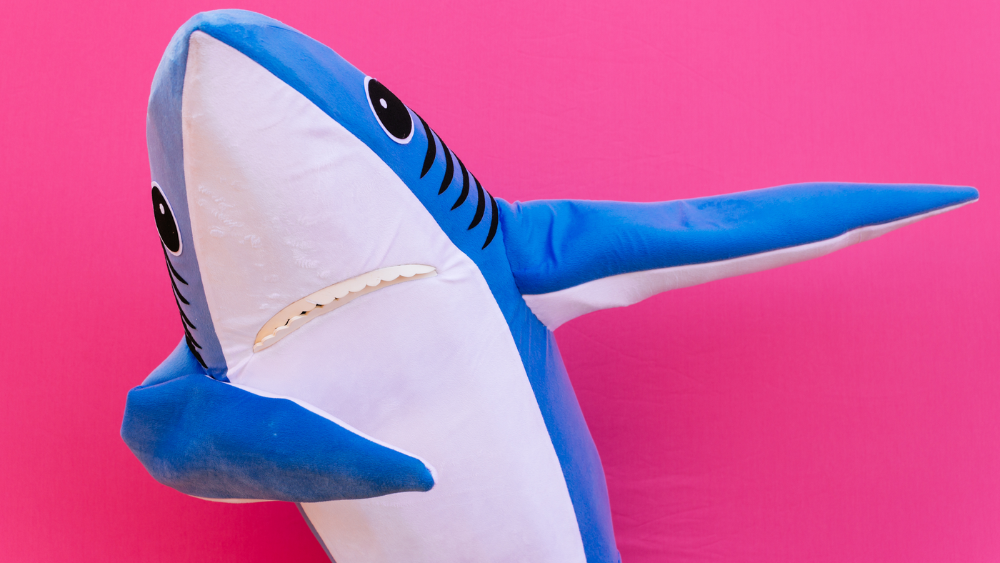 shark costume doing a dance on a pink background