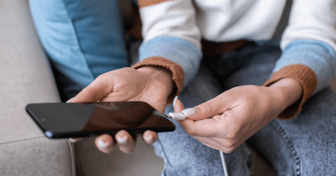 person inserting charging cable into bottom of black iphone