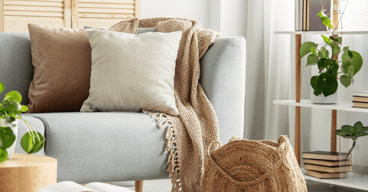 white and brown coloured cushions styled on grey sofa with beige colour blanket and plants in the background