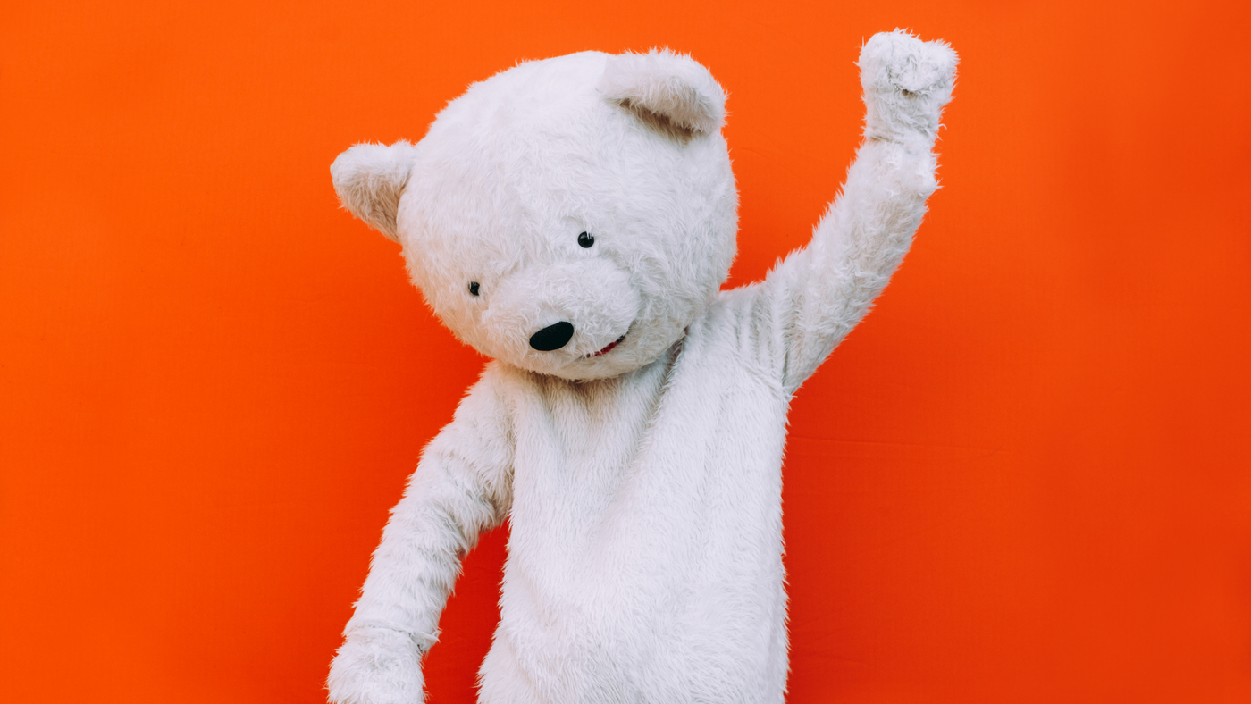 white teddy bear mascot costume holding hand up in celebration on orange background