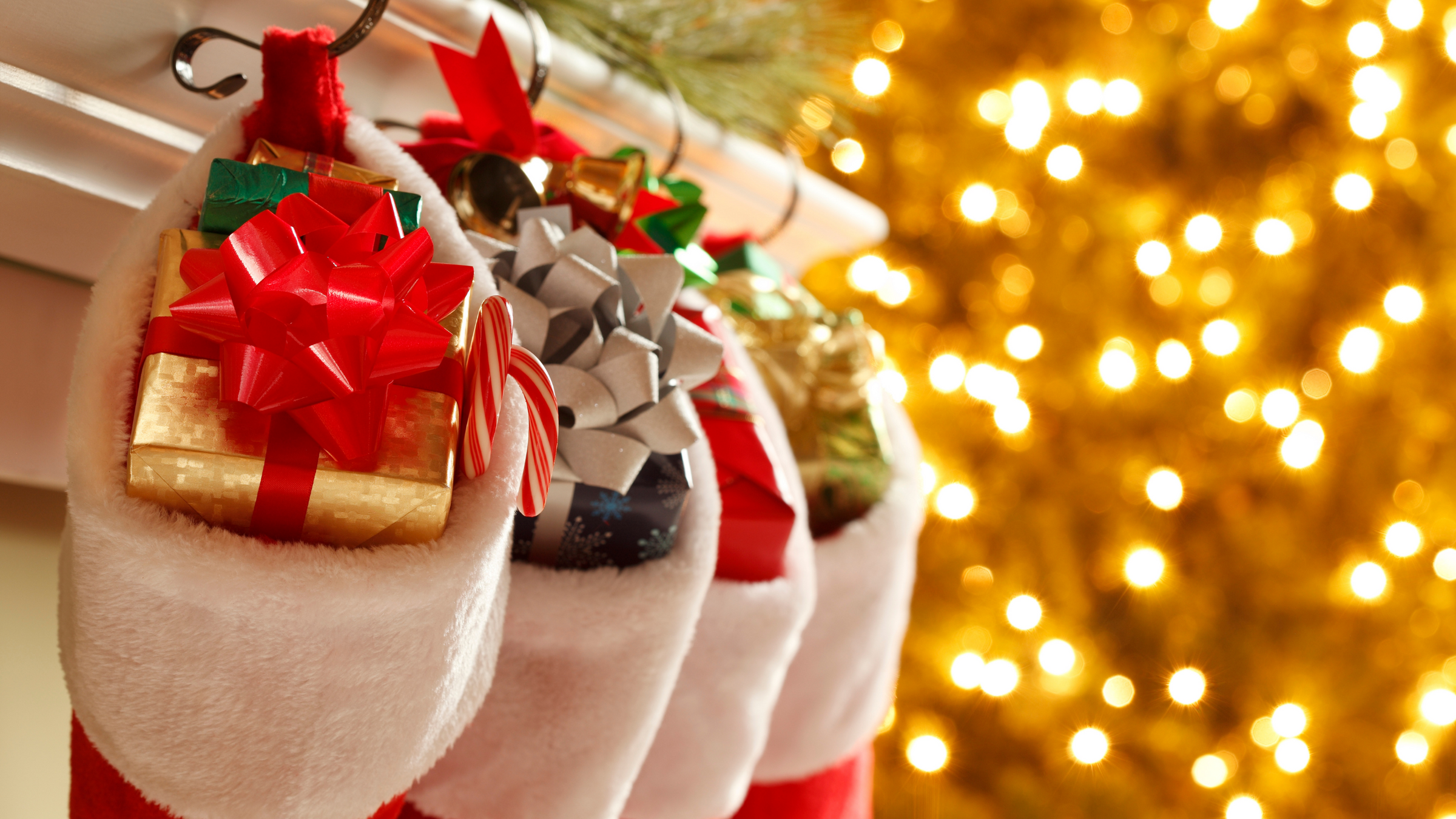 three christmas stockings in front of tree filled with gifts and candy canes