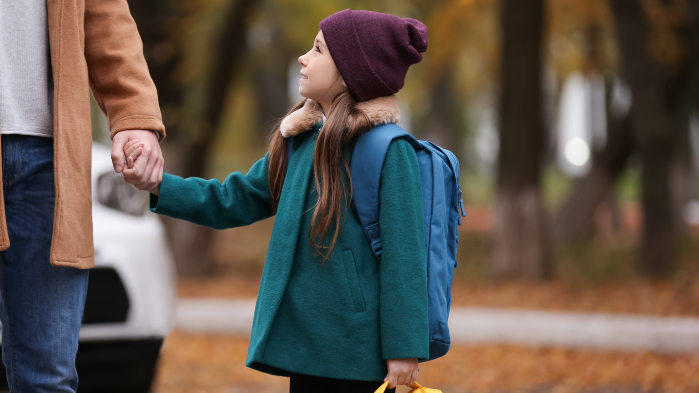 little girl walking to school holding Dad's hand, wearing green jacket with fur collar