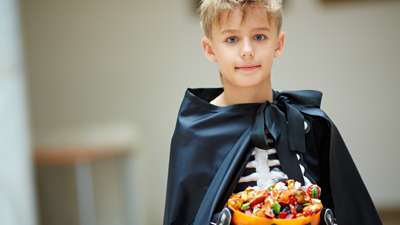 little boy holding his halloween candy and wearing a black cape