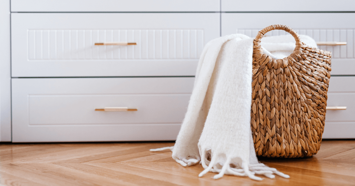 brown wicker laundry hamper with white cosy blanket throw inside infront of large white clothes drawers