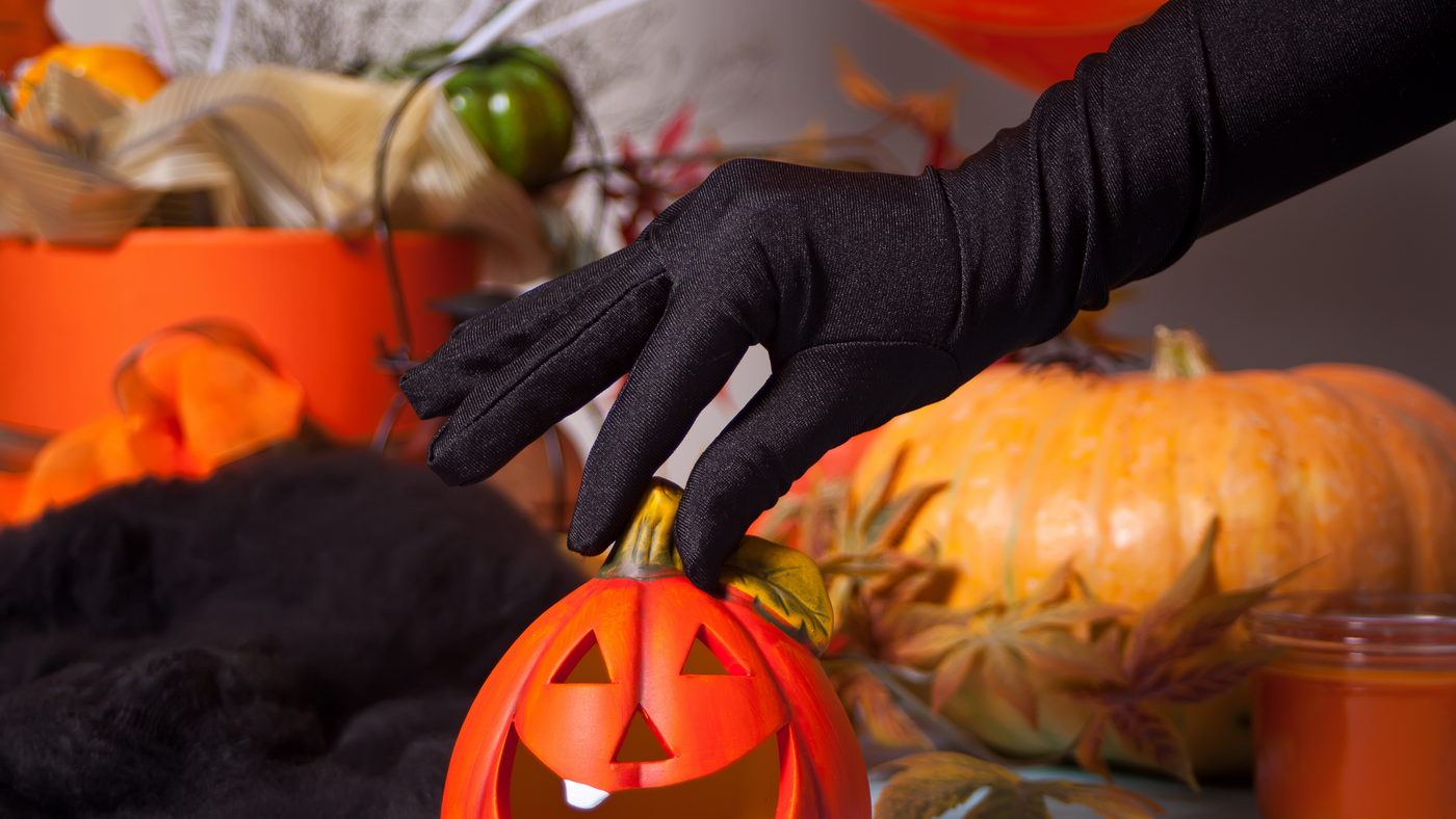 hand wearing long black glove reaching down to party table to pick up a mini pumpkin