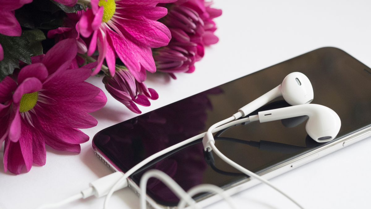 earphone on top of apple iphone beside pink flowers