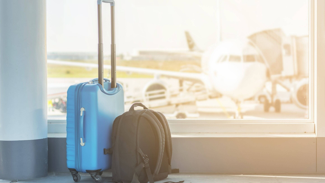 blue suitcase and business bag on floor at the airport with airplane in background