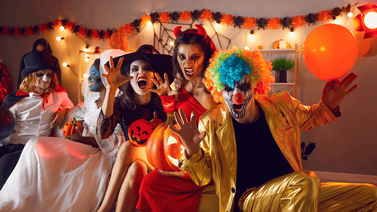 group of adult friends posing for the camera, wearing halloween costumes in a halloween decorated themed room party celebration