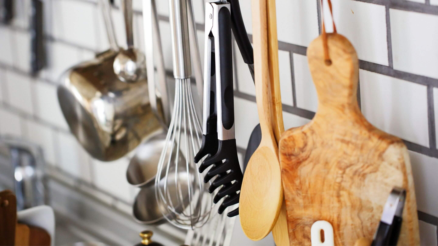 range of kitchen utensils hanging on the wall, including chopping board, whisk and stainless steel pot
