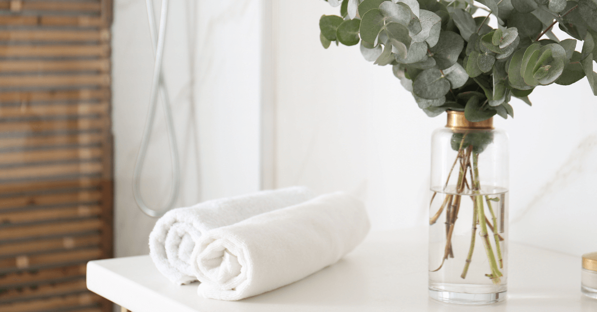 two white cotton bathroom towels on countertop beside eucalyptus flowers in bathroom