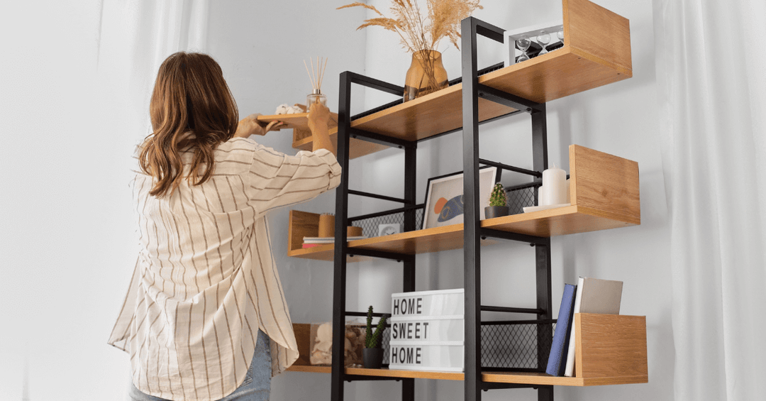 female in living room organising decor on industrial style shelf including light box, photo frames and vase with dried pampas stems