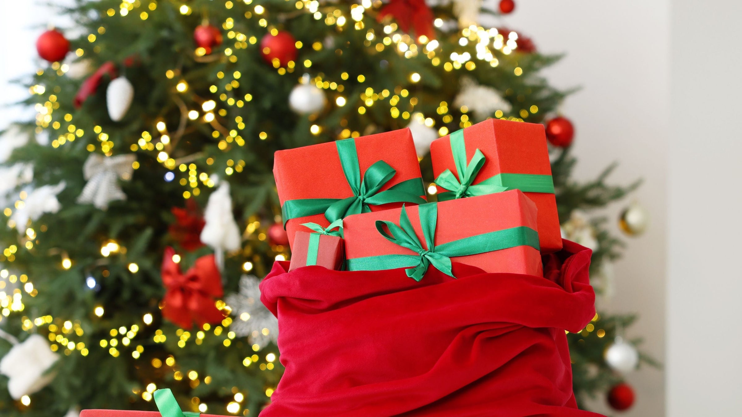 a red sack filled with christmas gifts in living room in front of christmas tree with gold and red baubles