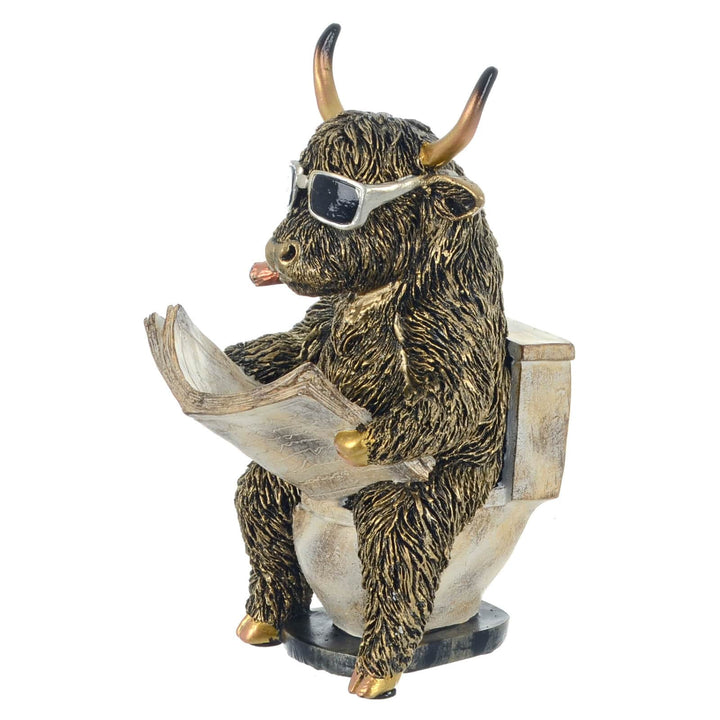 Funny Highland Cow figure with cigar and sunglasses on a toilet reading a newspaper