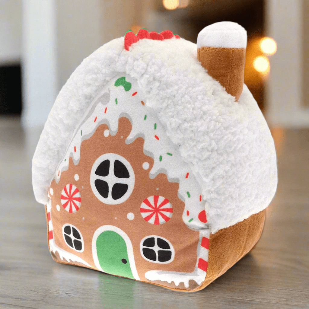 Gingerbread house-shaped door stopper on a wooden floor with a blurred background featuring door and christmas lights