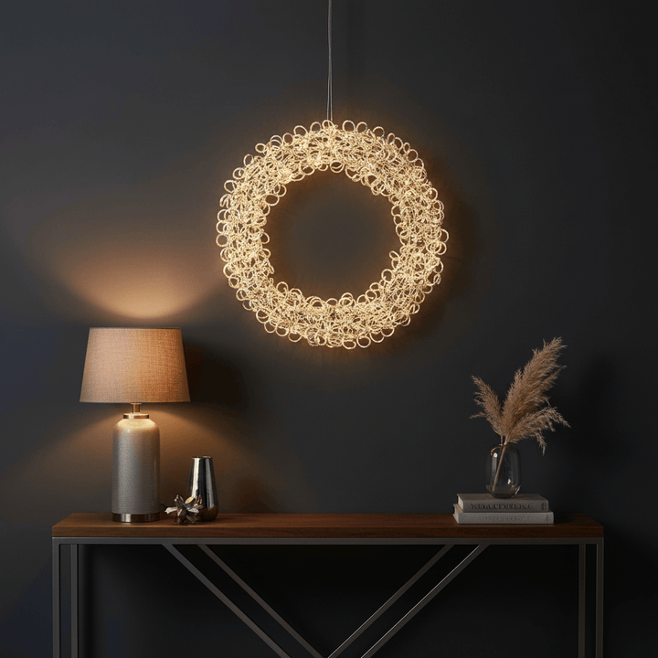 Decorative circular light fixture hanging above a wooden table with a lamp and vase.