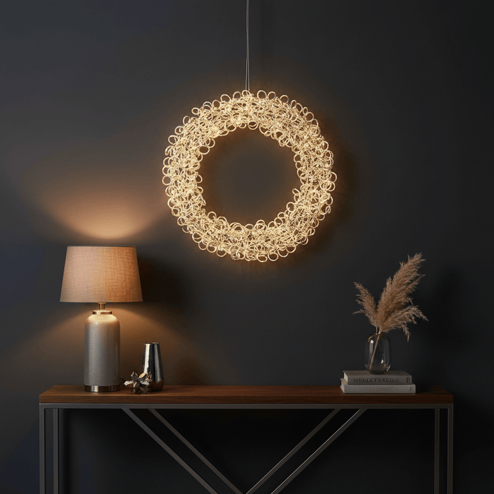 Decorative circular light fixture hanging above a wooden table with a lamp and vase.