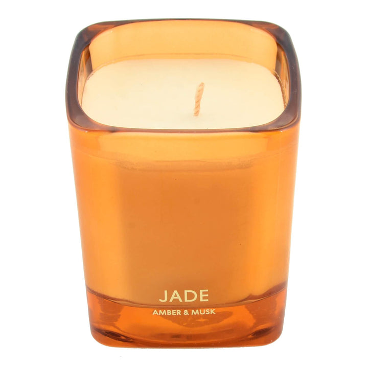Orange candle in a glass holder labeled &