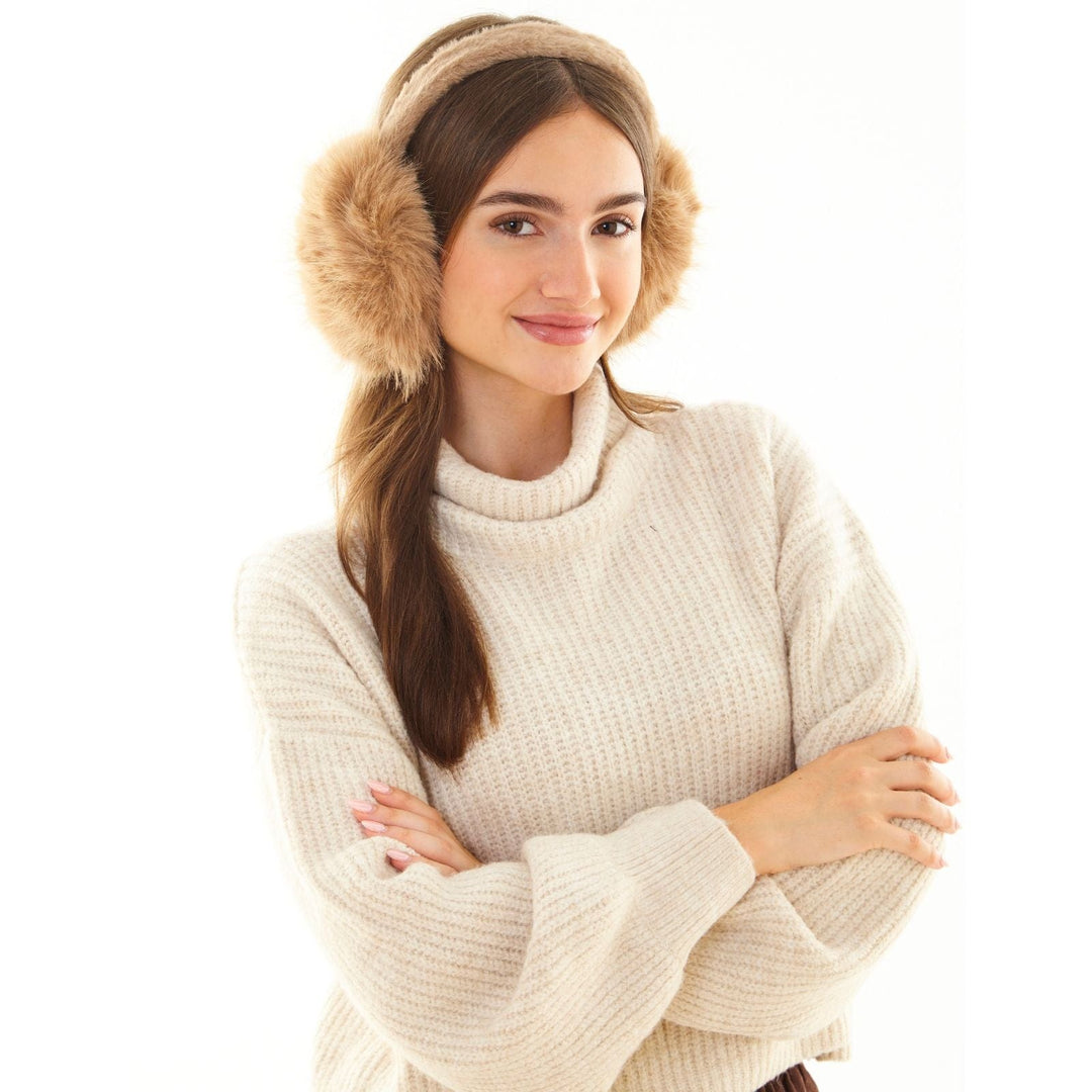 Woman wearing beige knitted sweater and fur ear muffs on a white background