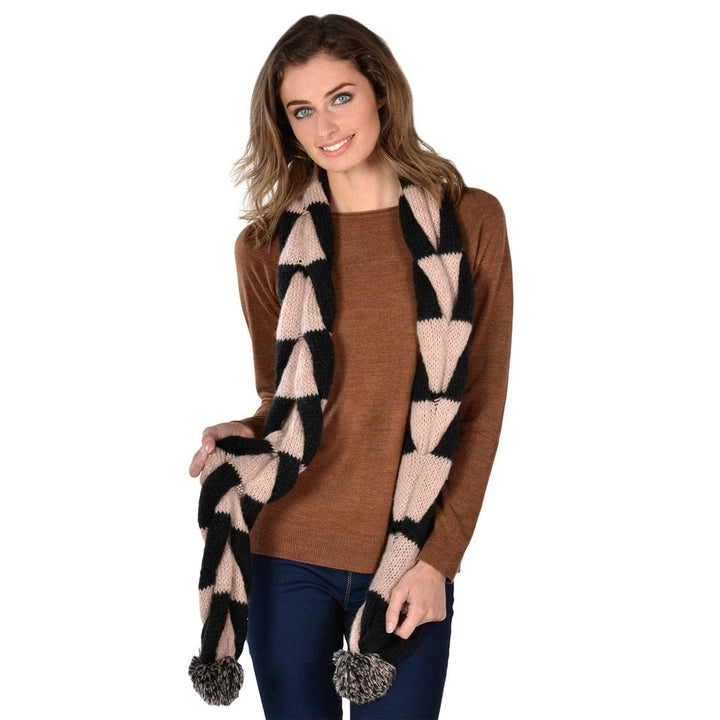 Woman wearing a brown jumper and a patterned black and beige scarf with pom-poms on a white background