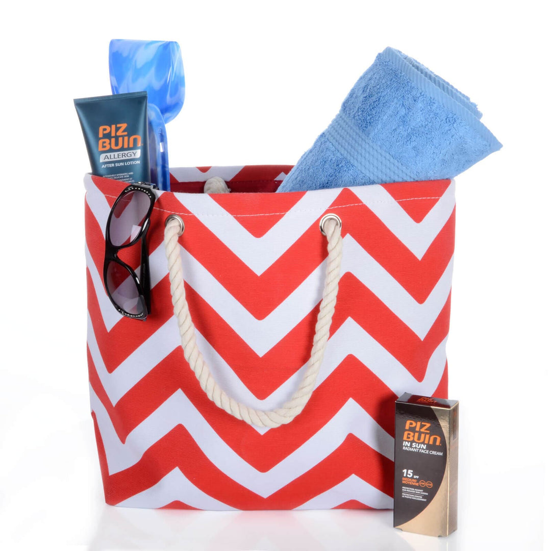 red and white chevron pattern beach bag with rope handles filled with towel and sun cream