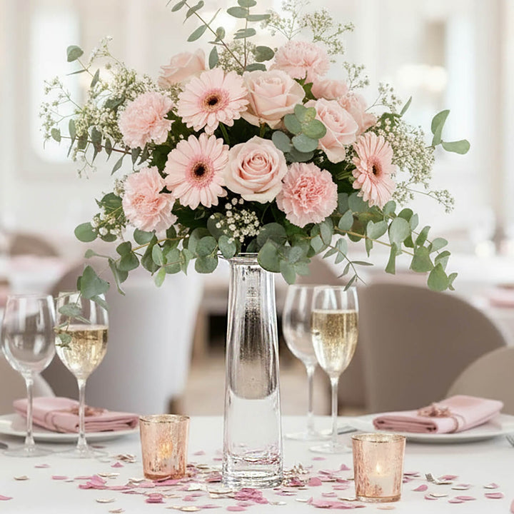Glass vase of pink flowers on a wedding table with champagne glasses and candles