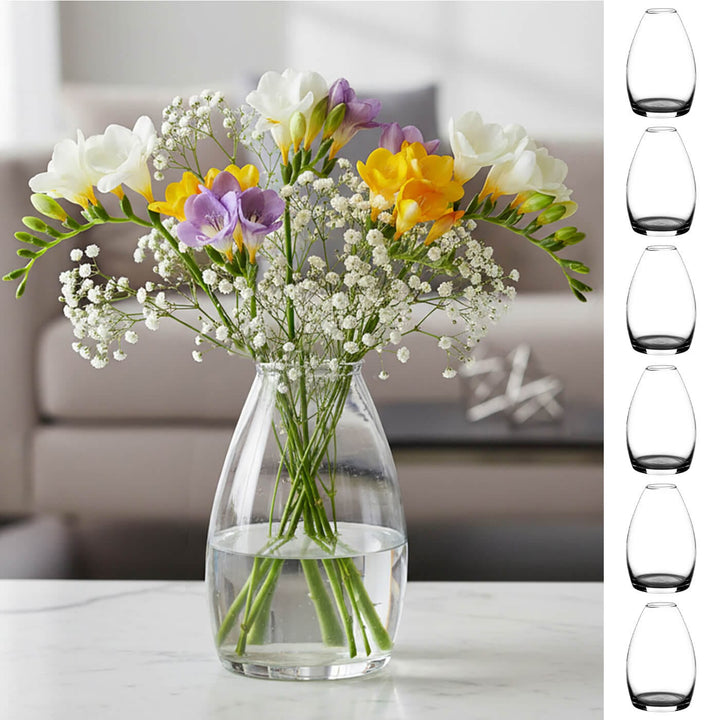 Clear glass vase with freesias and gypsophila on a table, with additional 6 clear glass vases displayed to the right.