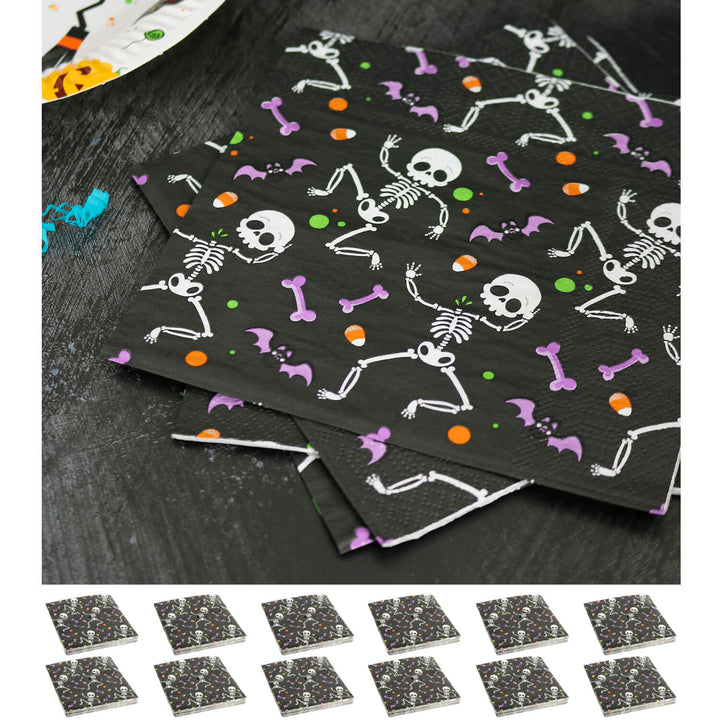 Black paper napkins with Halloween-themed designs including skeletons, bones, and pumpkins on a dark surface.