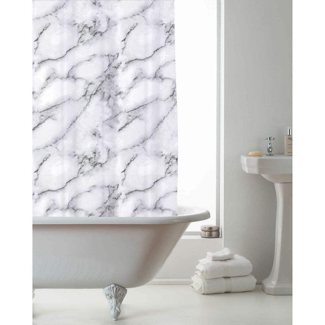 A white marble-patterned shower curtain hanging over a white clawfoot bathtub in a bright bathroom with a pedestal sink and folded white towels.