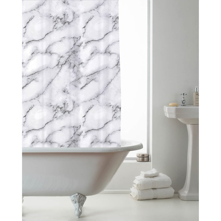 A white marble-patterned shower curtain hanging over a white clawfoot bathtub in a bright bathroom with a pedestal sink and folded white towels.