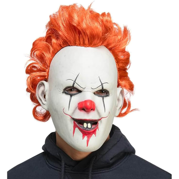 A Pennywise clown mask with bright orange hair, worn by a model in a black hoodie against a plain white background.
