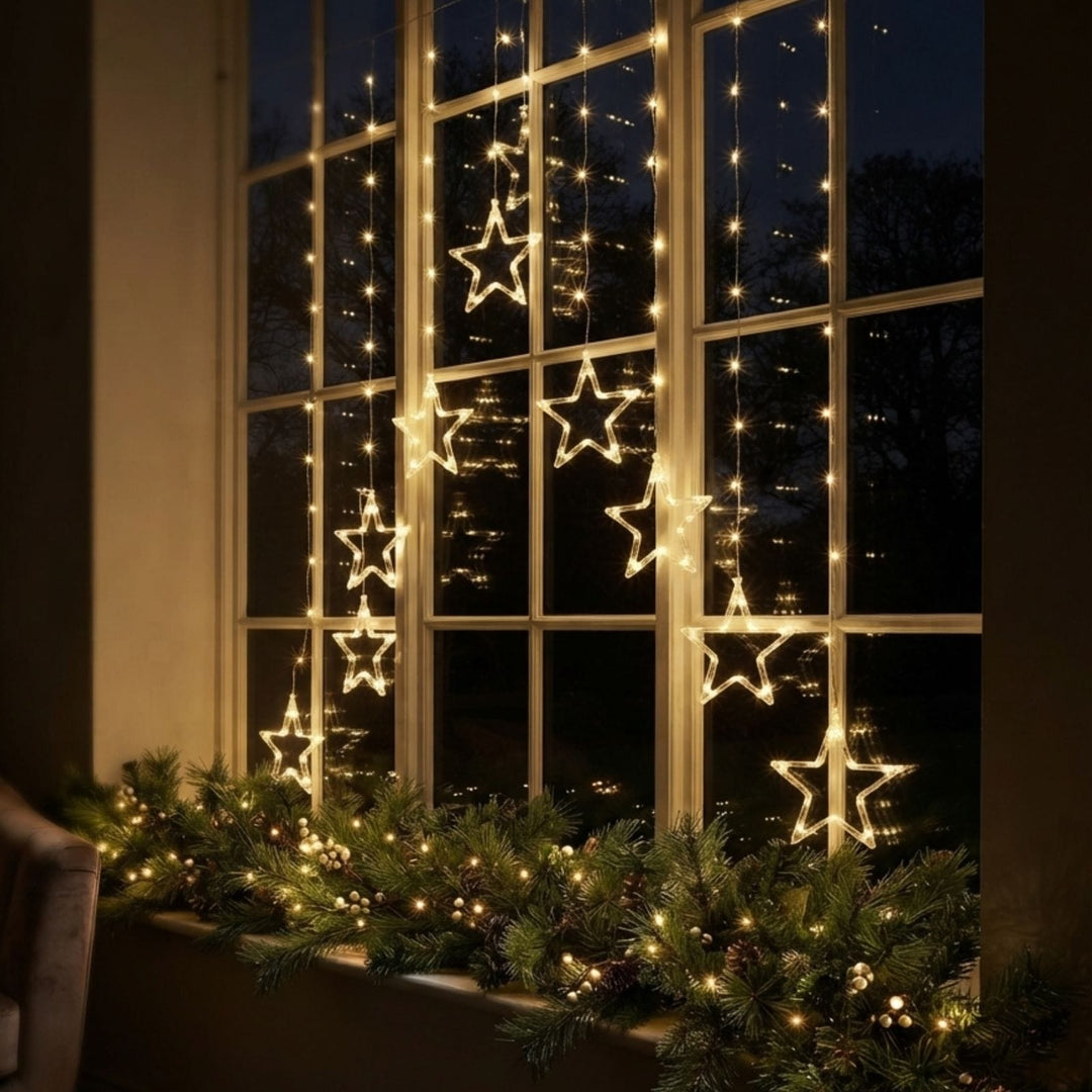Warm white LED star string lights hanging on a large window, with a green garland of similar lights draped along the window sill.