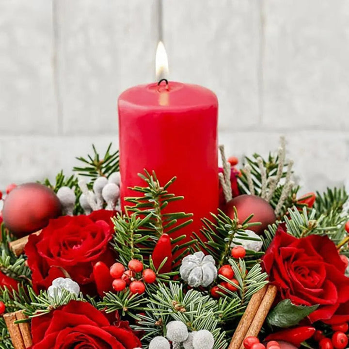 Red pillar candle in a Christmas floral display with pine and red roses