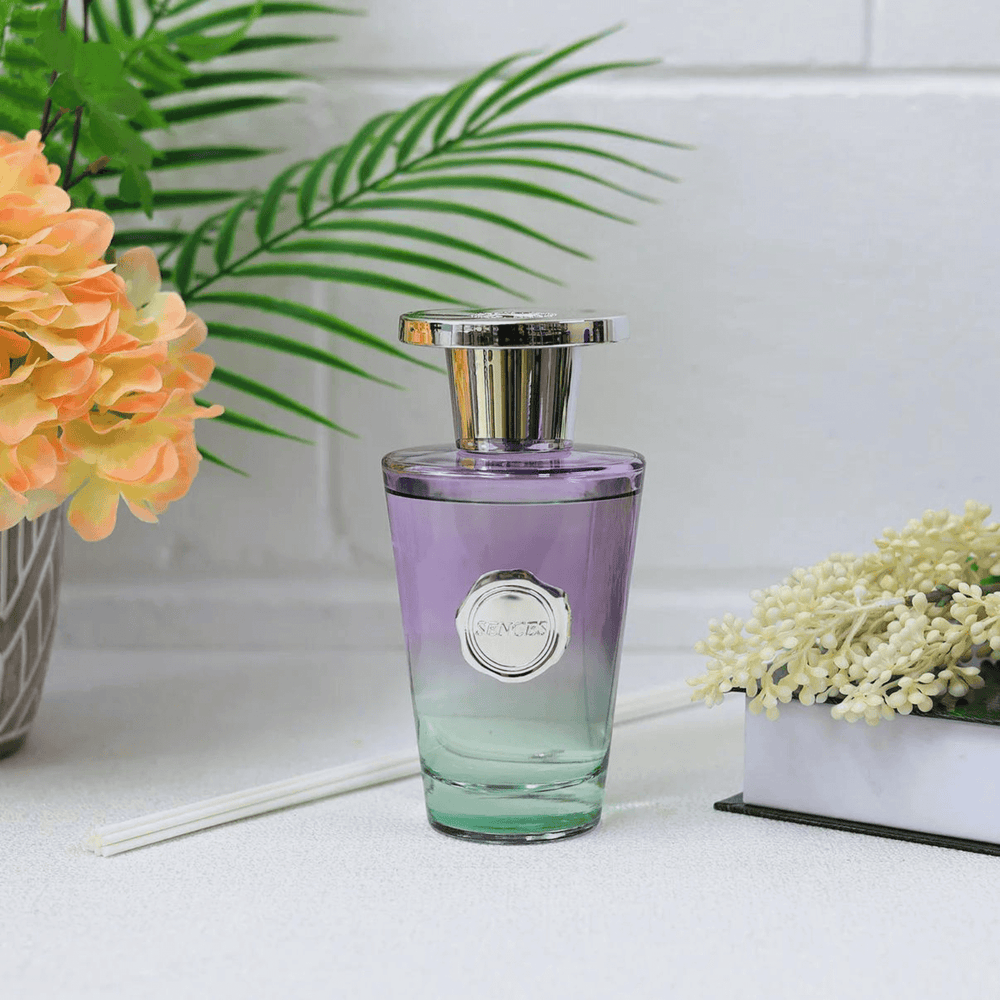 green and purple ombre glass bottle on white worktop beside orange flowers and a book