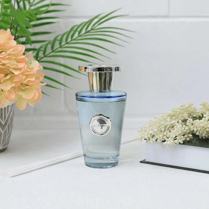 blue reed diffuser bottle on white worktop beside orange flowers and white reeds