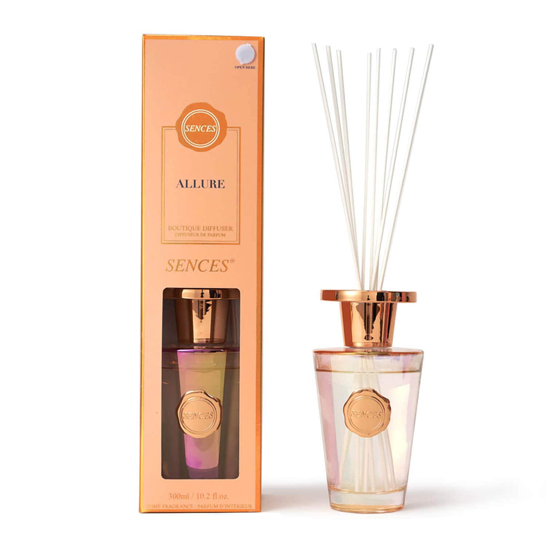 Sences Allure reed diffuser set with a peach-colored box, a clear glass bottle containing iridescent pink liquid, and white reeds, shown on a white background.