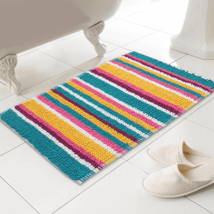 bright multi coloured striped bobble bath mat on bathroom floor beside white waffle slippers