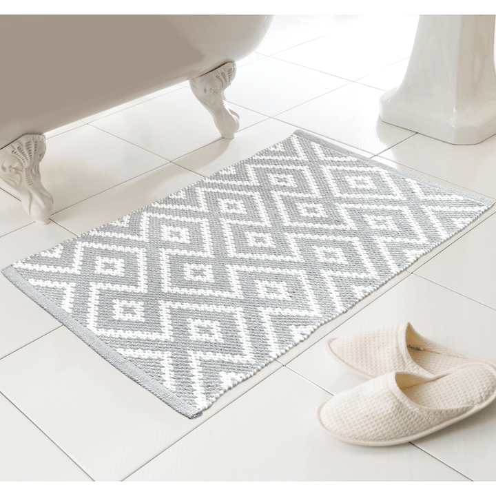 grey geometric bath mat on bathroom floor beside slippers and bath