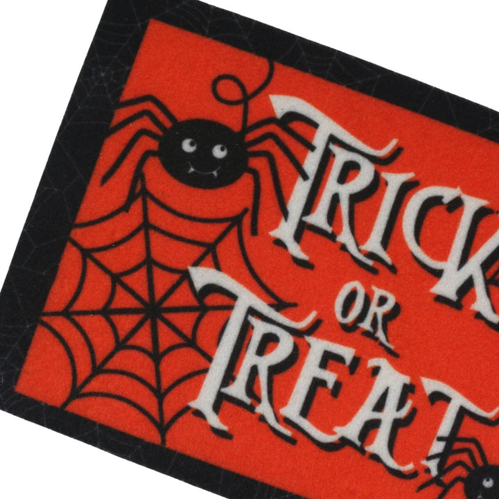 A close-up of a Halloween-themed decorative mat with a bright red background, black spider and spiderweb graphics, and large white gothic text reading &