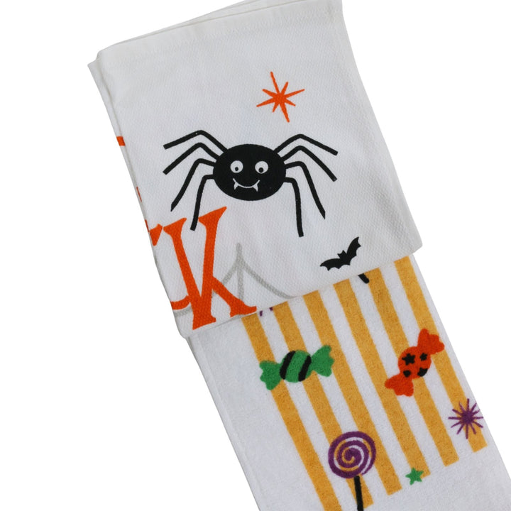 A white kitchen towel with a Halloween theme, featuring a black spider, orange stars, a bat, candy, and a striped section with orange and yellow.