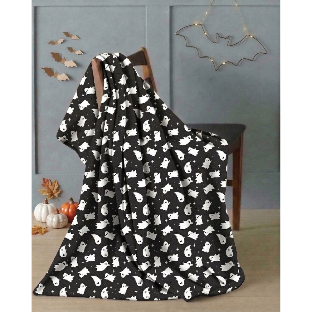 A black blanket with a white cartoon ghost pattern draped over a wooden chair in a styled room setting with Halloween decorations.